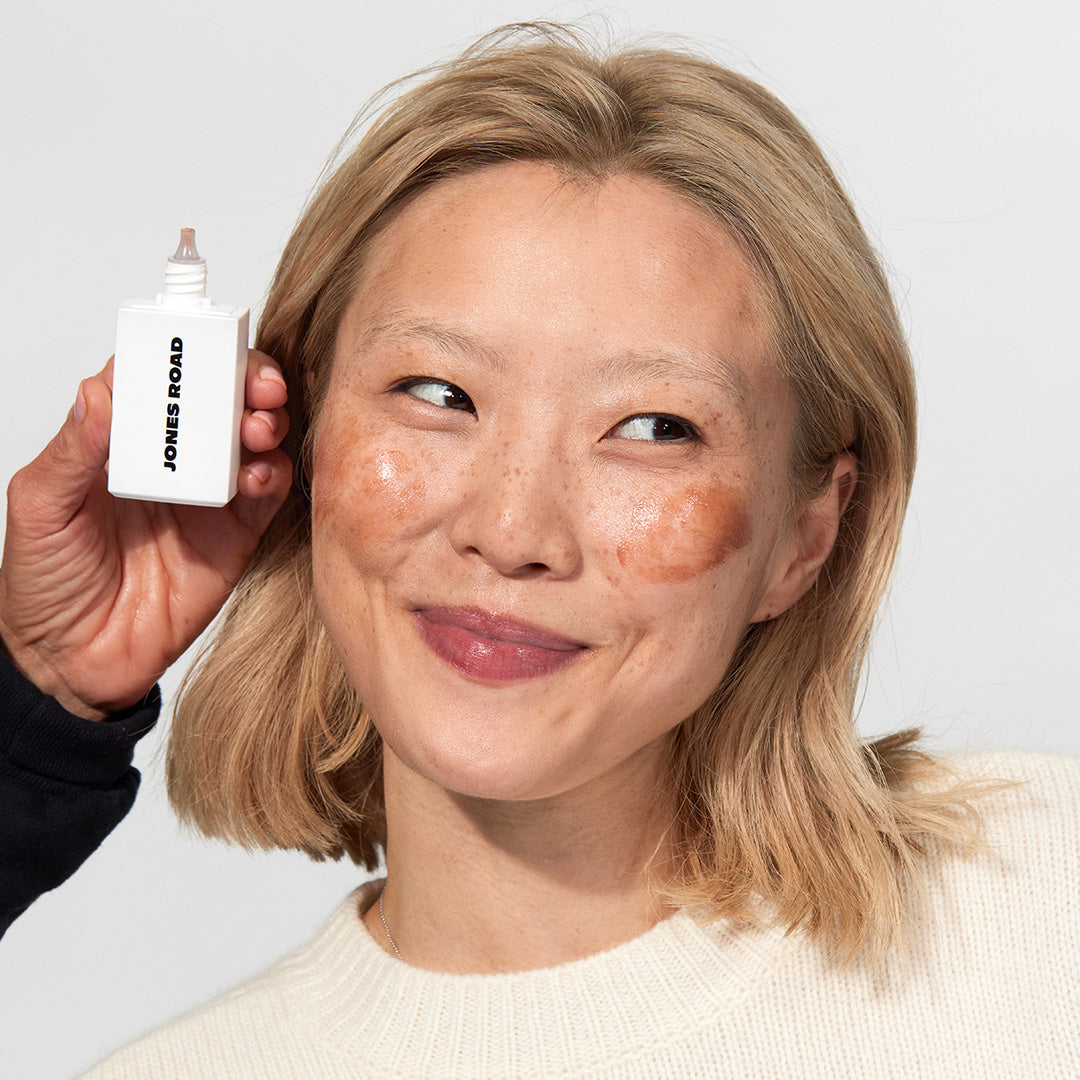 A woman wearing The Gel Bronzer from Jones Road Beauty before rubbing it in to show the color of the bronzer