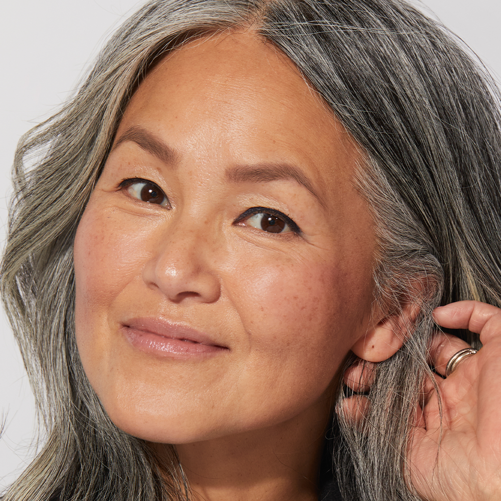 A woman with gray hair wearing Jones Road Beauty's Lip and Cheek Stick in Bright Pink
